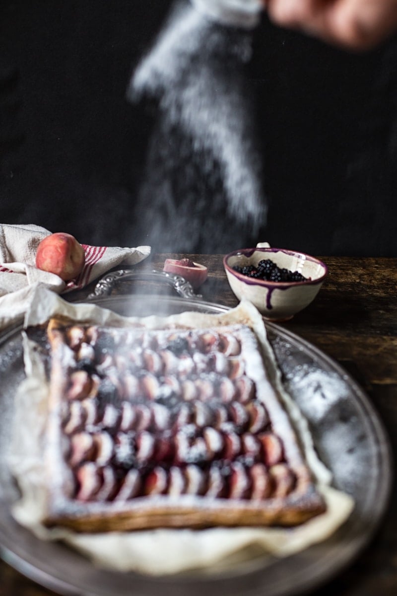 Icing sugar being sprinkled on the peach and blackberry tart