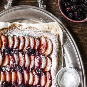 Corner of the tart next to icing sugar and blackberries
