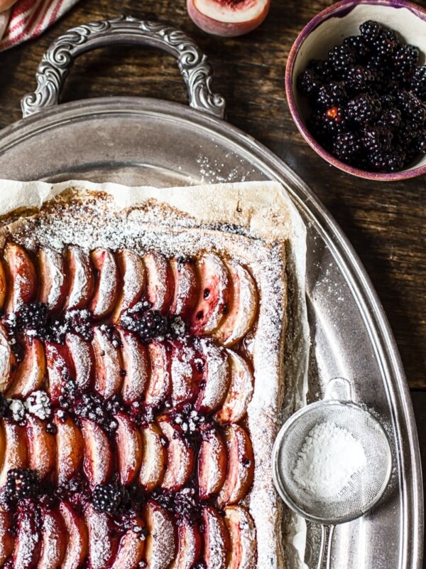 Corner of the tart next to icing sugar and blackberries