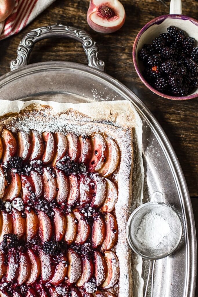 Corner of the tart next to icing sugar and blackberries