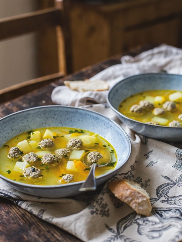 Two bowls of meatball soup on a table with a piece of bread