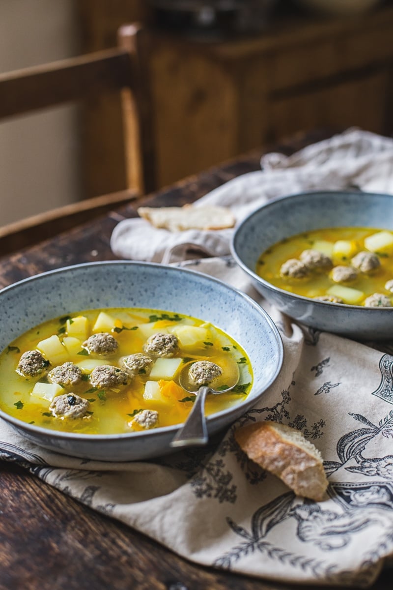 Two bowls of meatball soup on a table with a piece of bread