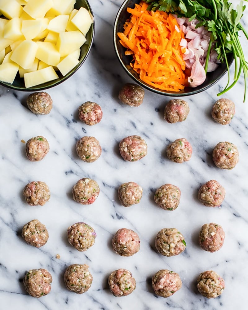 Soup ingredients in bowls along with meatballs arranged on marble table