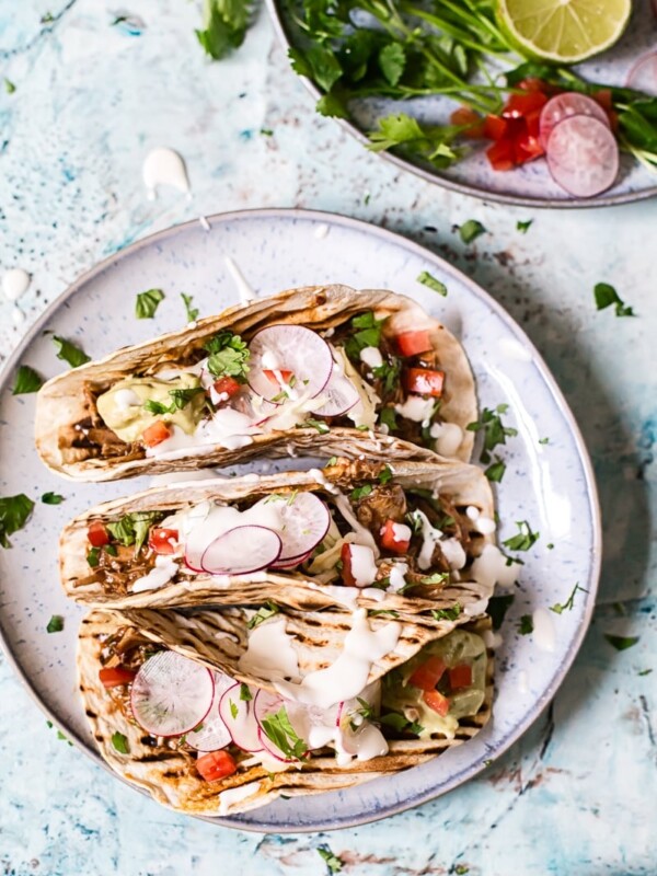 three tacos on a plate with fillings including vegetables and sauces