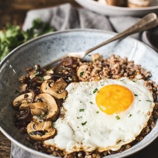 Buckwheat with mushrooms and fried egg in a bowl with a fork