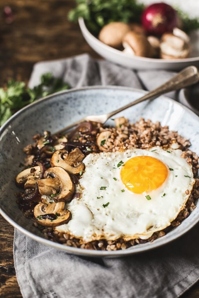 Buckwheat with mushrooms and fried egg in a bowl with a fork