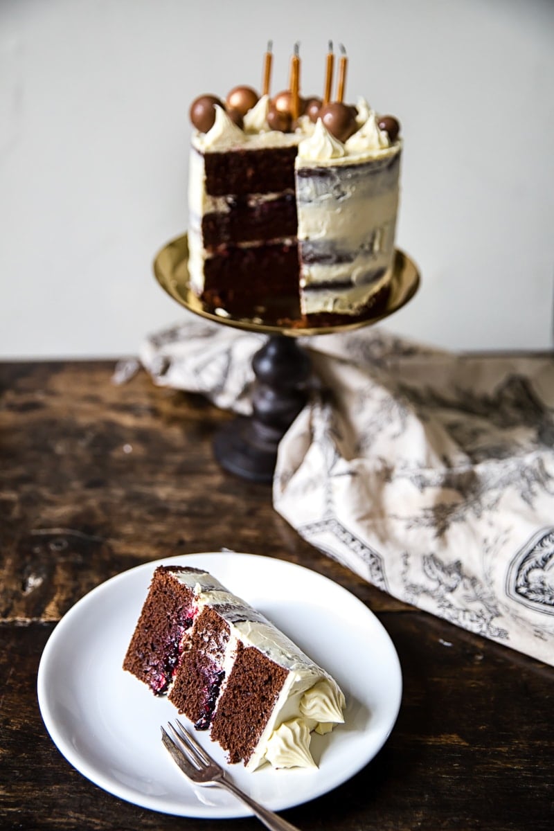 Black and white cake on a stand with slice removed onto a plate