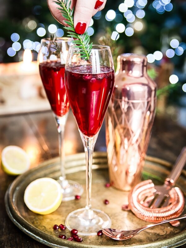 Two glasses with the cocktail with hand adding clipped pine branch