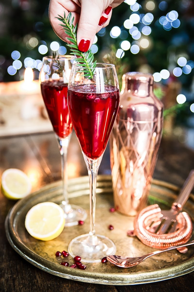 Two glasses with the cocktail with hand adding clipped pine branch