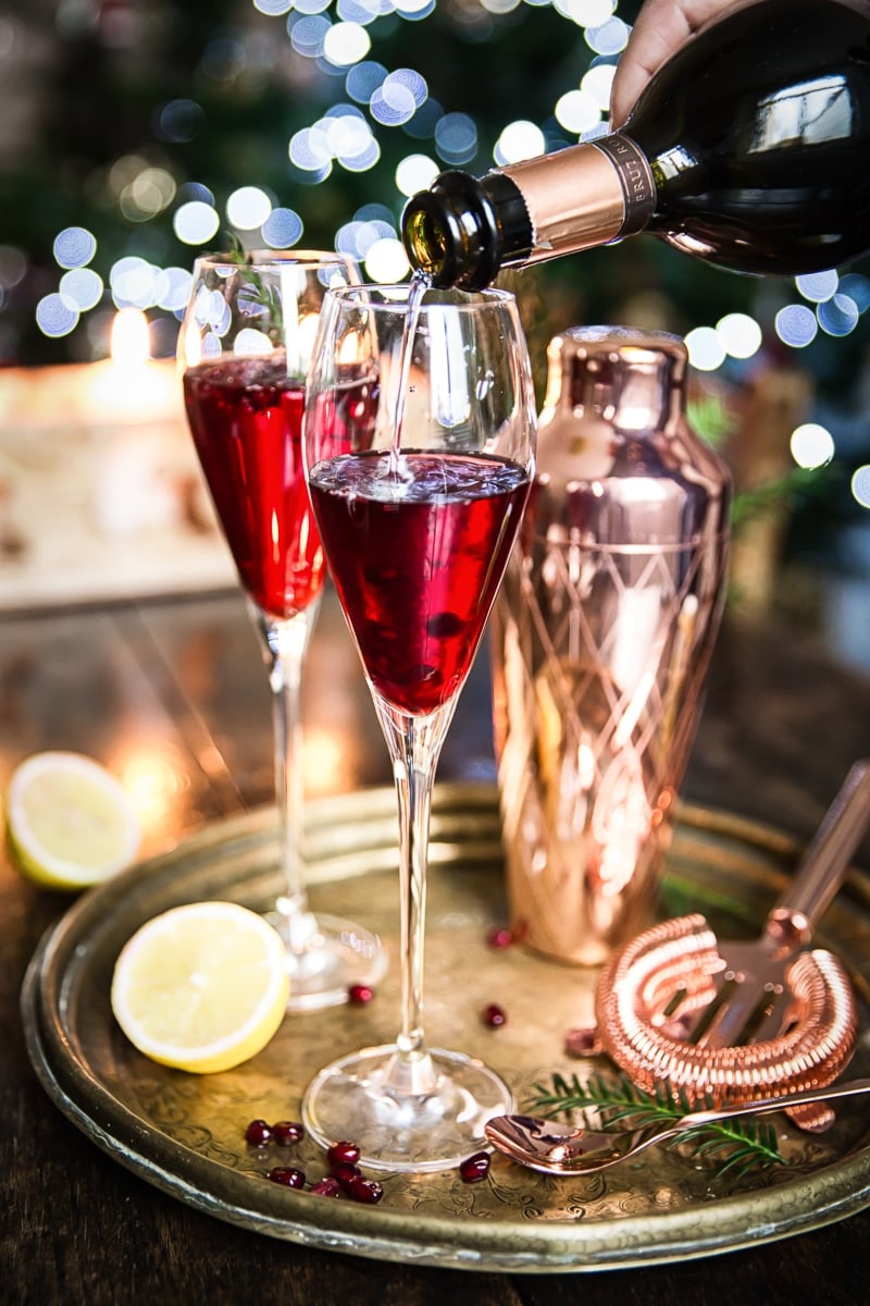 Two champagne glasses with Pomegranate French 75 being topped with champagne