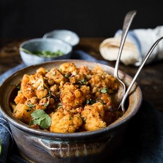 aloo gobi in a clay pot with extra herbs in the background