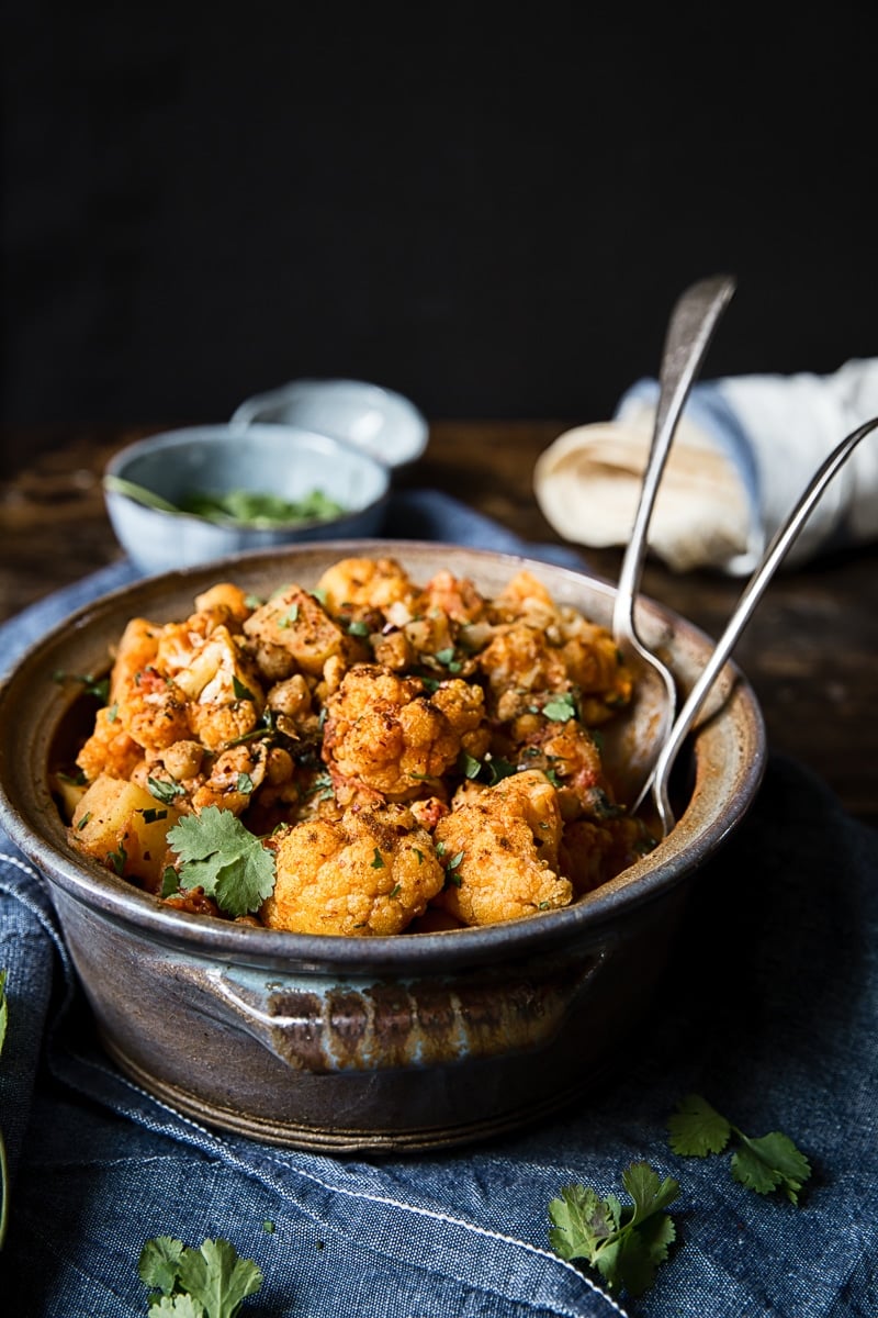 aloo gobi in a clay pot with extra herbs in the background