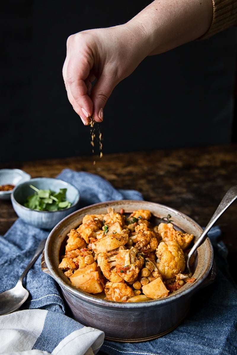 hand dropping spice onto cauliflower and potato curry