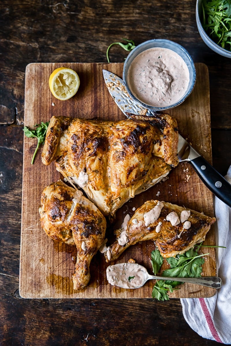 Spatchcocked Chicken in Spicy Yogurt Sauce on a cutting board with knife