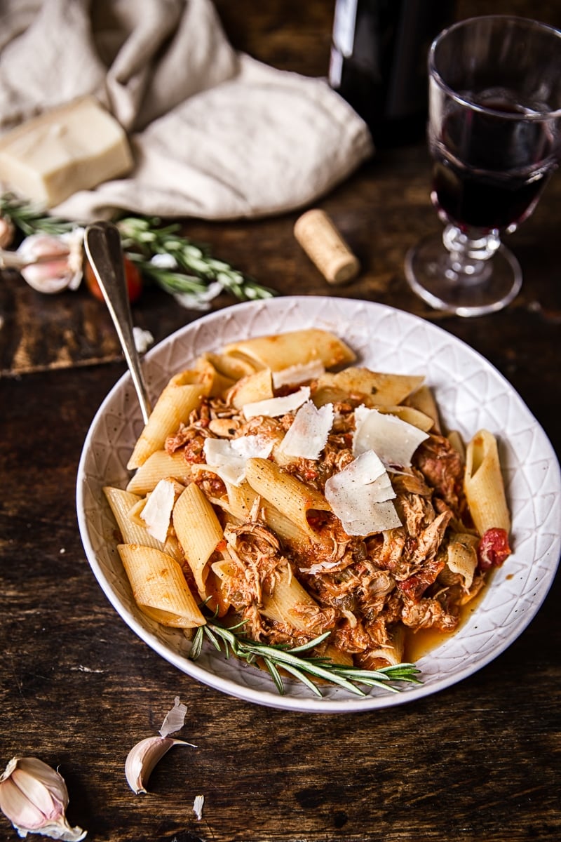 Bowl of chicken ragu pasta on a wooden table with a glass of wine