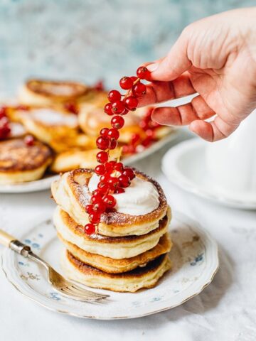 Hand adding red berries to stack of pancakes