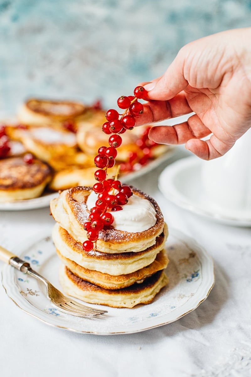 Hand adding red berries to stack of pancakes