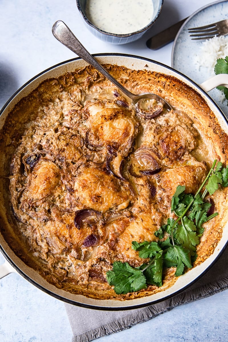 Top down view of spiced chicken thighs braised in milk in a pan with side plates