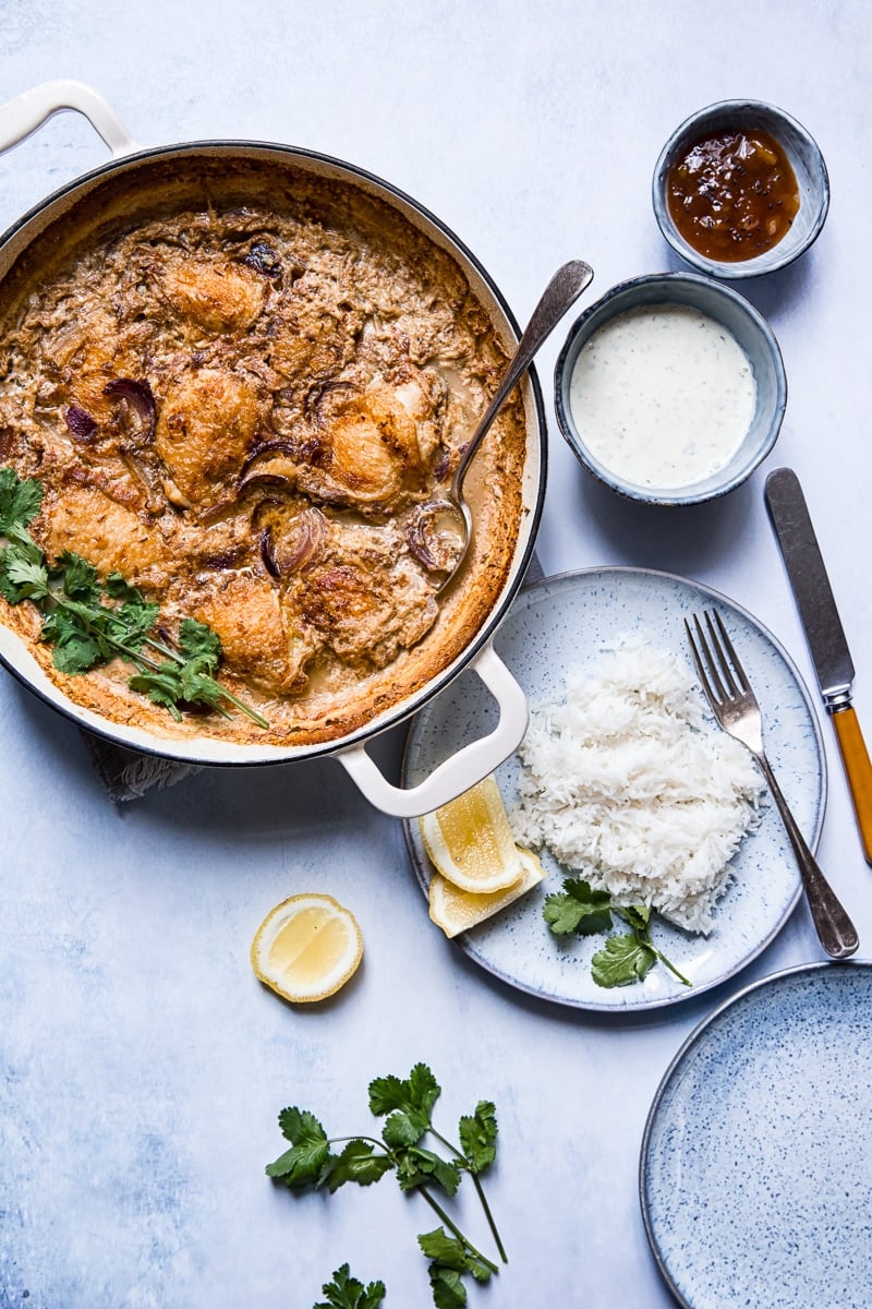 Spiced Chicken Thighs Braised in Milk in a pan next to a plate of rice and extra sauces