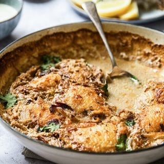 Side view of a pan with the spiced chicken thighs with spoon in the broth