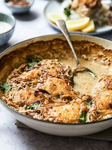 Side view of a pan with the spiced chicken thighs with spoon in the broth