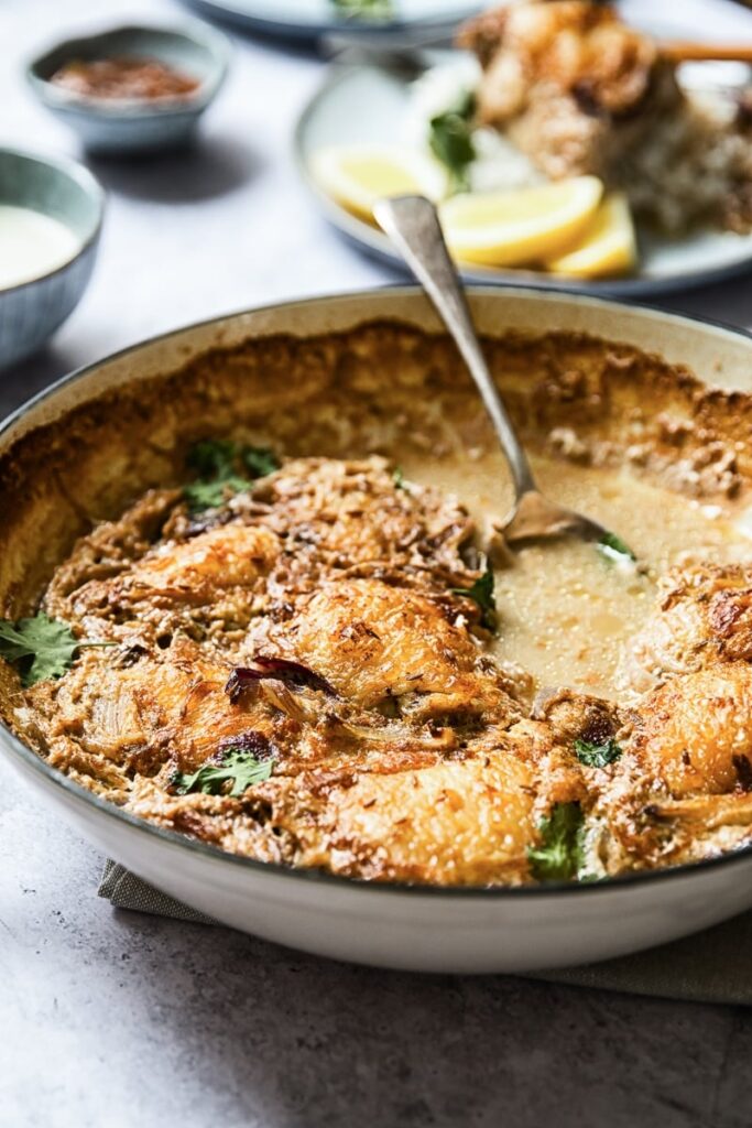 Side view of a pan with the spiced chicken thighs with spoon in the broth