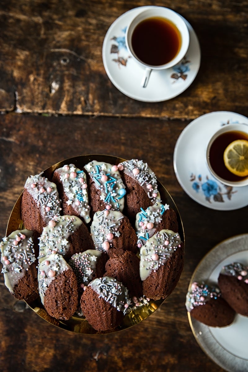 Top down of a plate of Chocolate Madeleines with cups of tea