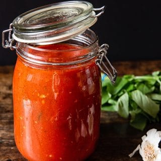 Jar of red sauce next on a wooden table with garlic and basil