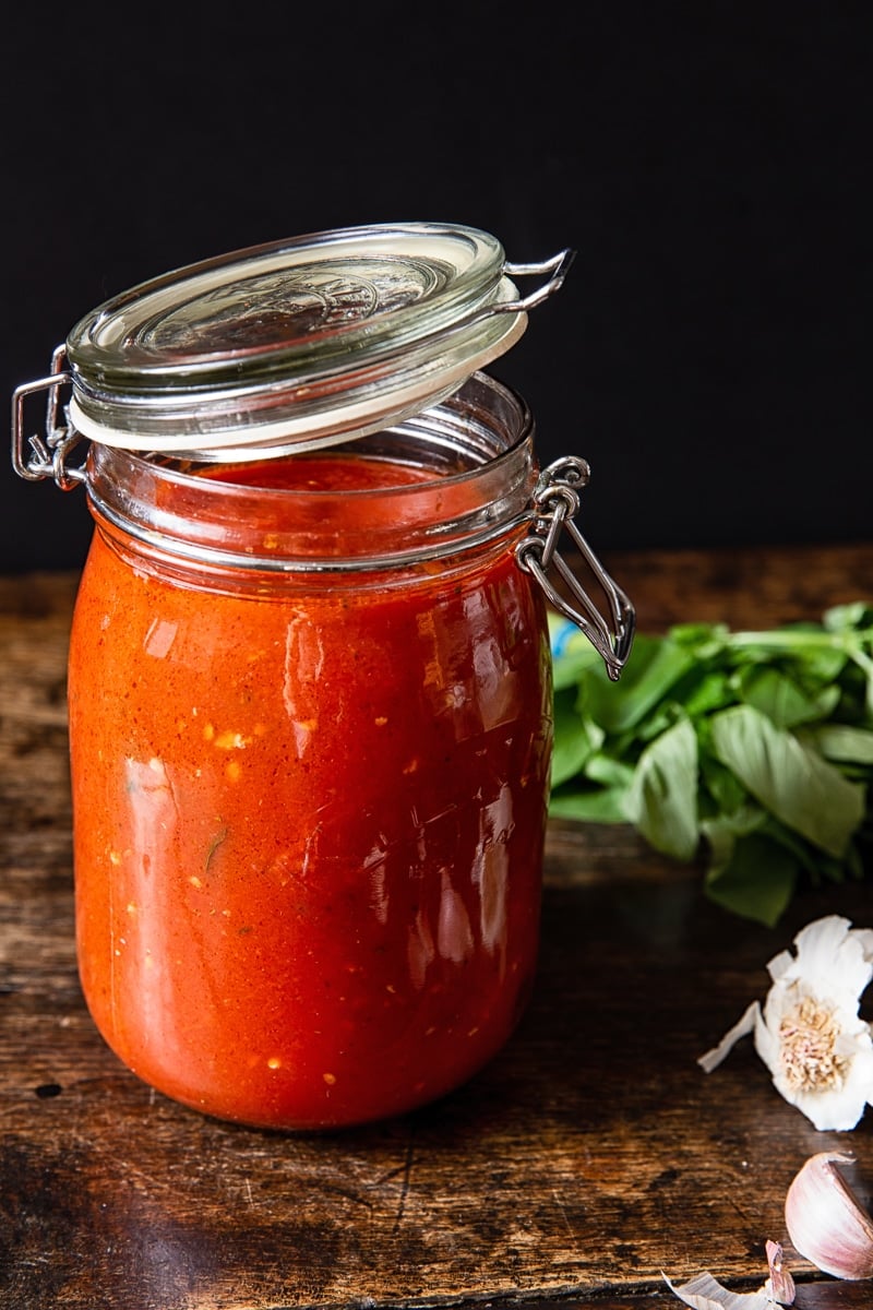 Jar of red sauce next on a wooden table with garlic and basil