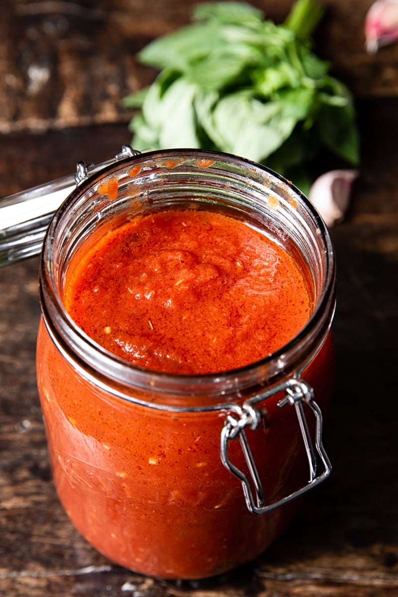 Open jar full of spaghetti sauce with fresh basil in the background