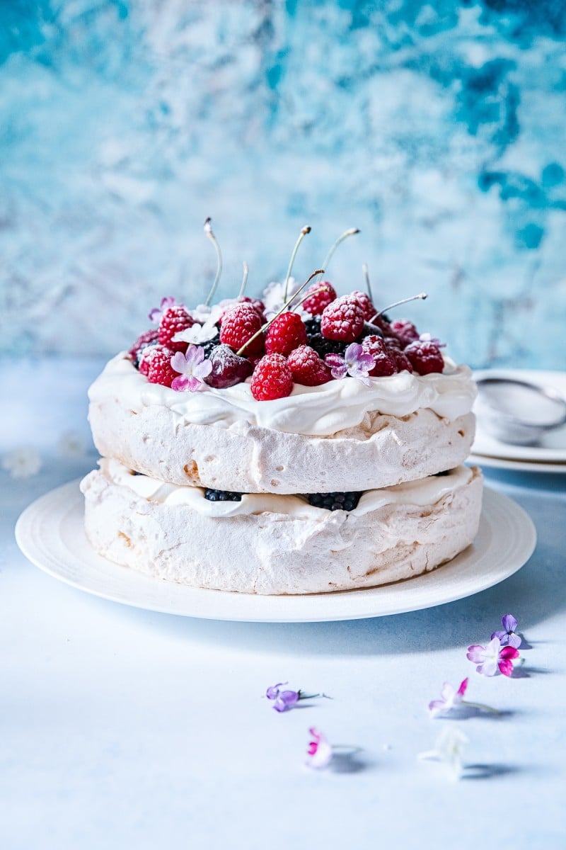 Double Stacked Berry Pavlova on a plate with a blue background