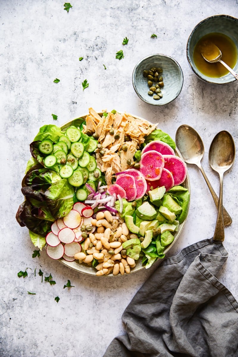 Top down view of tuna salad with bowls of capers and dressing