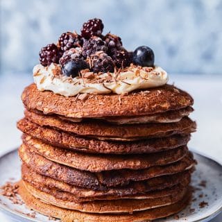 a stack of buckwheat pancakes, topped with whipped cream and berries