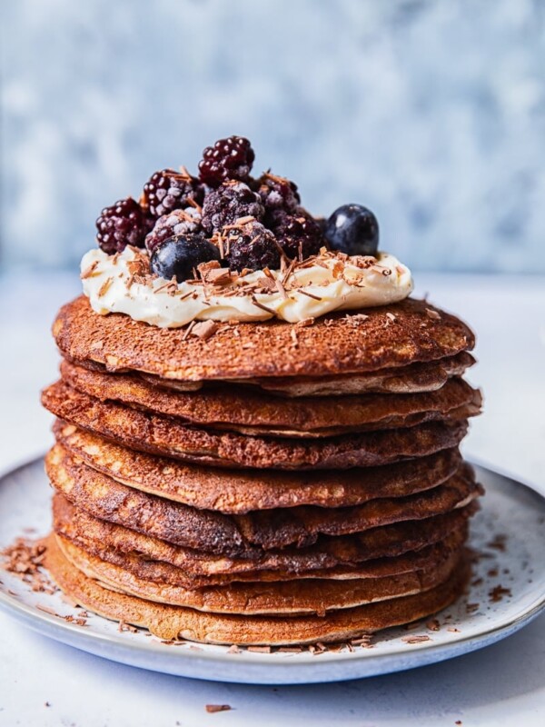 a stack of buckwheat pancakes, topped with whipped cream and berries