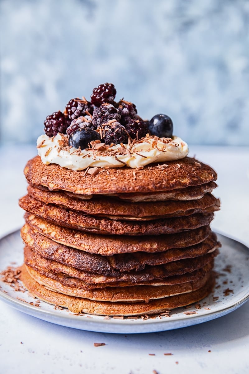 a stack of buckwheat pancakes, topped with whipped cream and berries