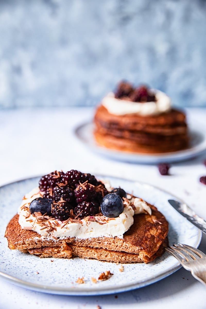 two pancakes on a light blue plate with a portion cut off, another plate with pancakes in the background