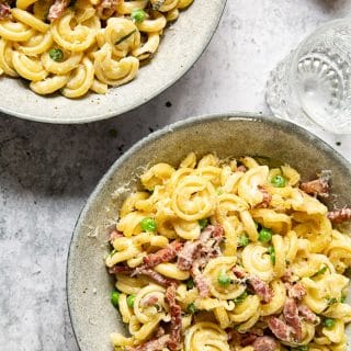 top down view of two bowls of pasta with pancetta and peas with water glass