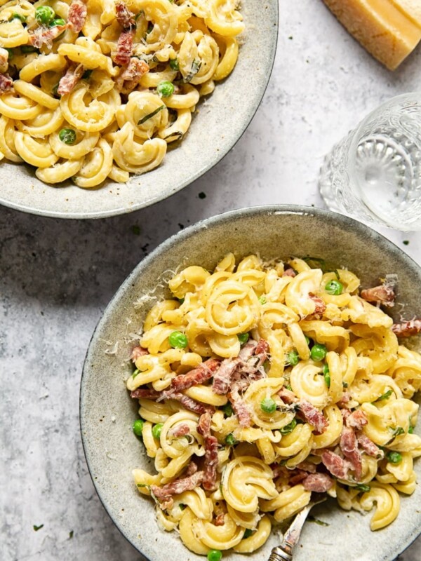 top down view of two bowls of pasta with pancetta and peas with water glass