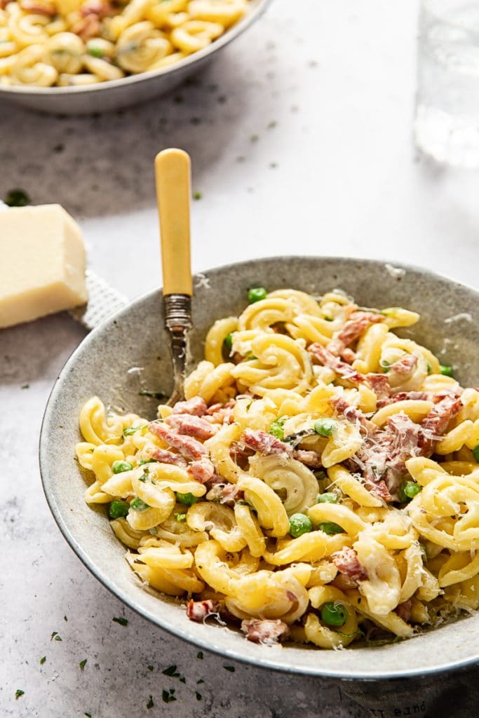 Bowl of Creamy Pasta with Peas and Pancetta with a fork inserted