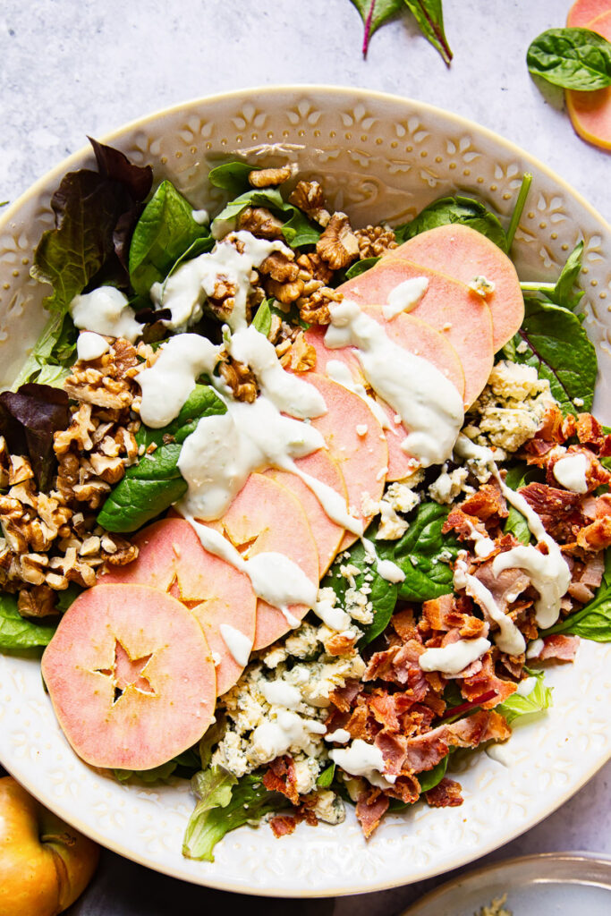 Bowl of salad with apples arranged across and topped with a white dressing.