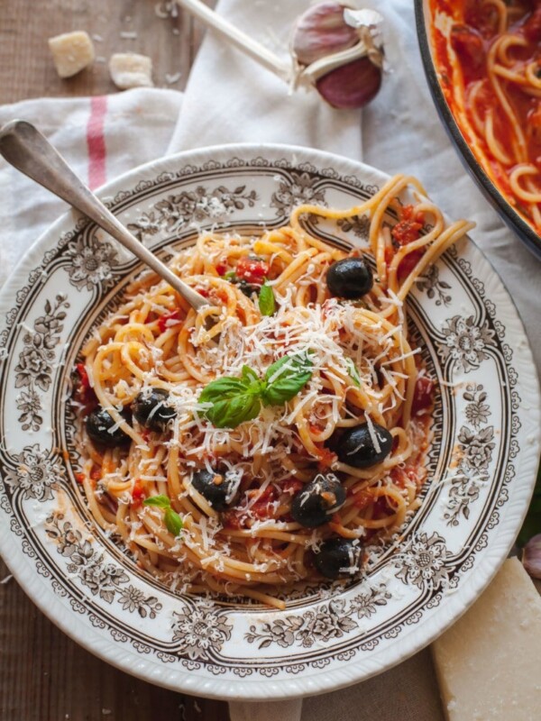 top down view of spaghetti topped with black olives, parmesan cheese and fresh basil