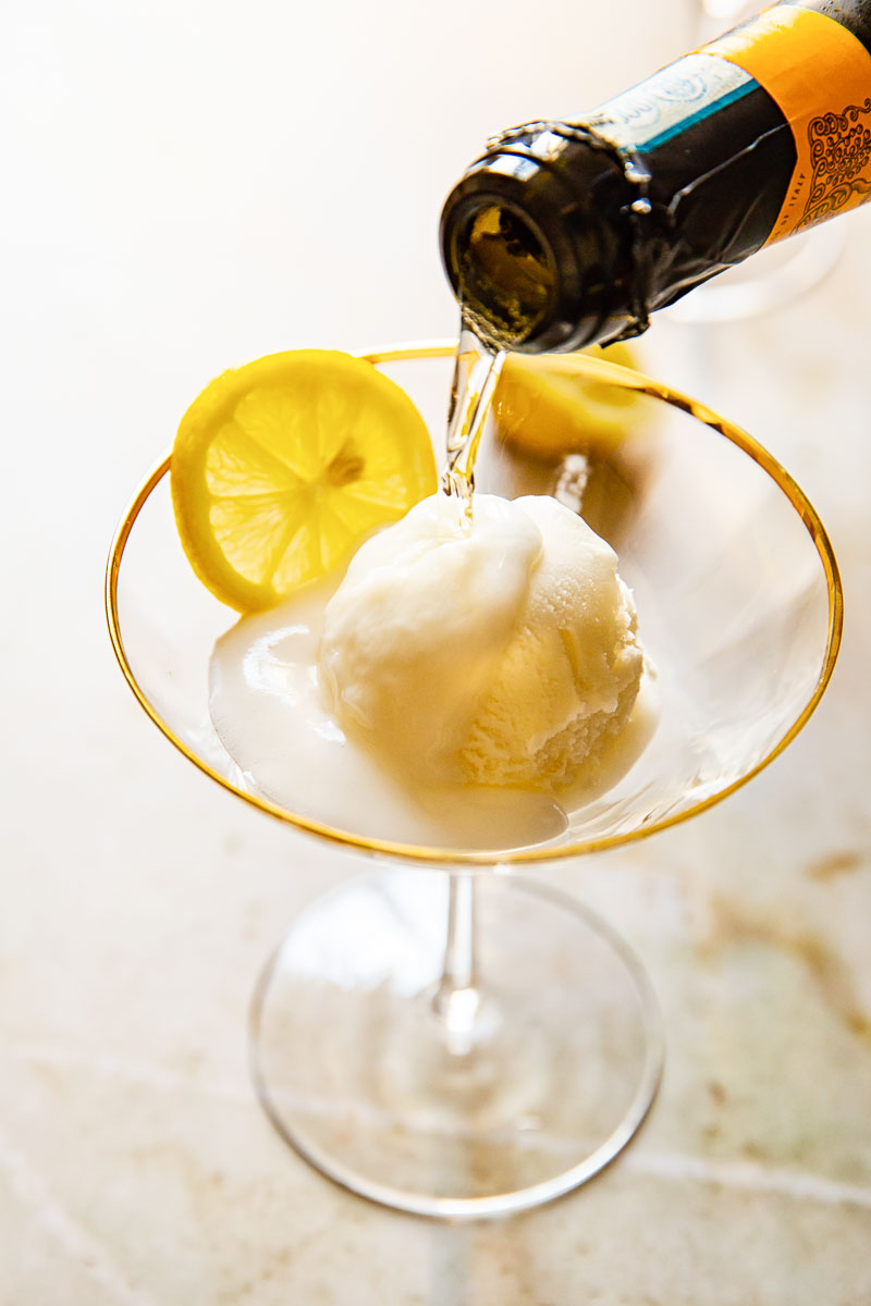 bottle neck pouring prosecco into cocktail glass with sorbet and lemon slice