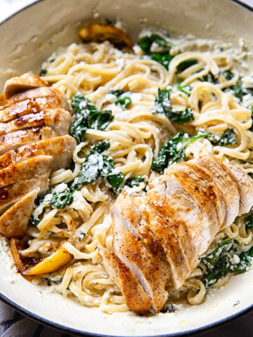 Spinach ricotta linguine with sliced lemon butter chicken in white pan