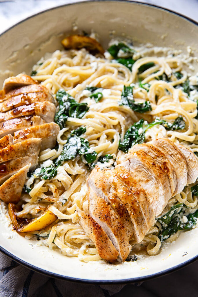 Linguine in sauce with sliced lemon butter chicken in white pan