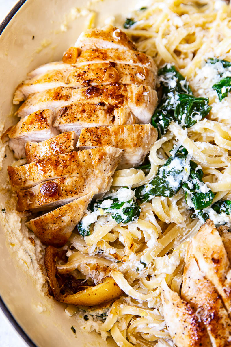 Sliced lemon butter chicken breasts on top of spinach ricotta pasta