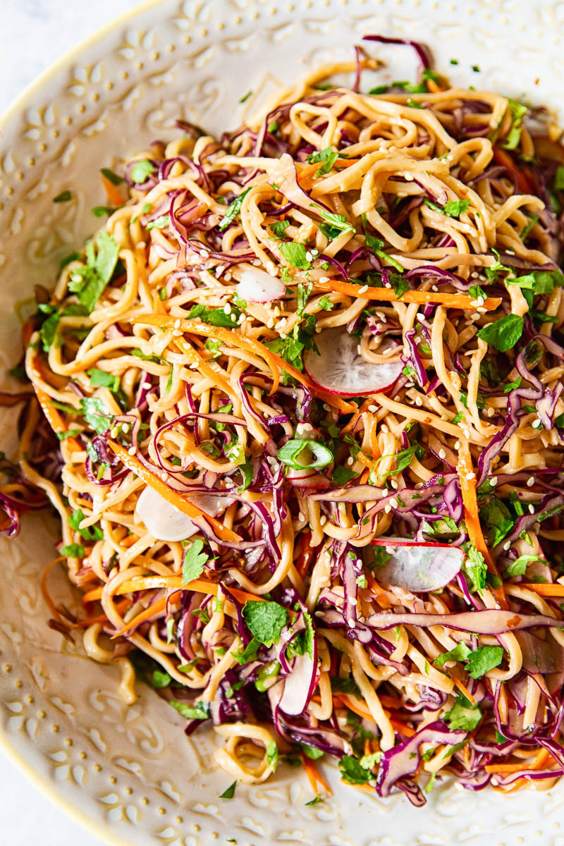 Asian noodle salad with red cabbage, carrots and radishes, sprinkled with green onions and sesame seeds.