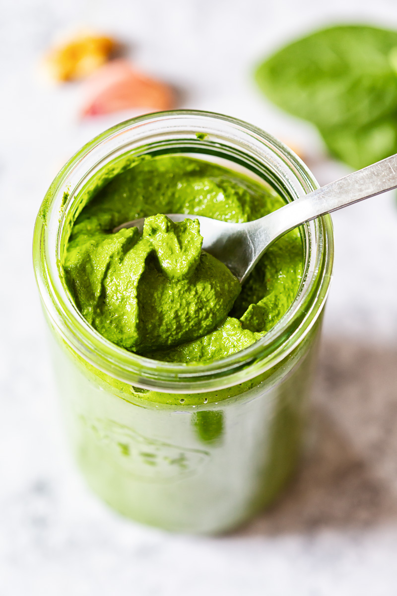 Spinach pesto on a spoon in glass jar. View from top. 