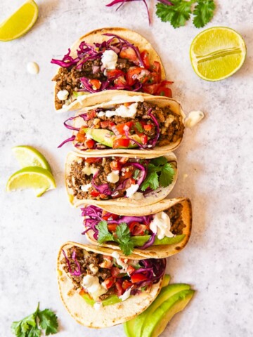 Ground Beef Tacos topped with salsa, avocado slices and red cabbage slaw.