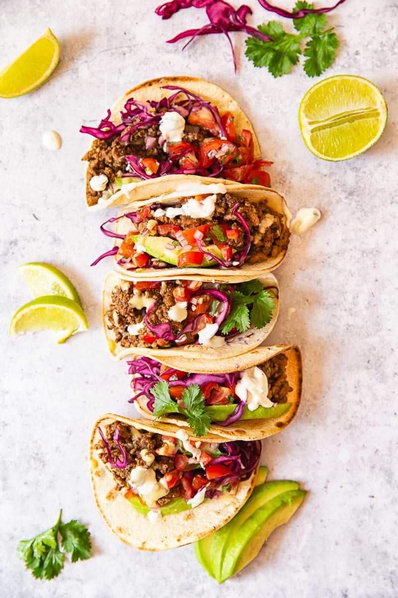 Ground Beef Tacos topped with salsa, avocado slices and red cabbage slaw.