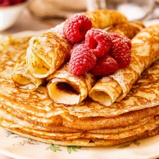Blini stacked on a plate, topped with raspberries.